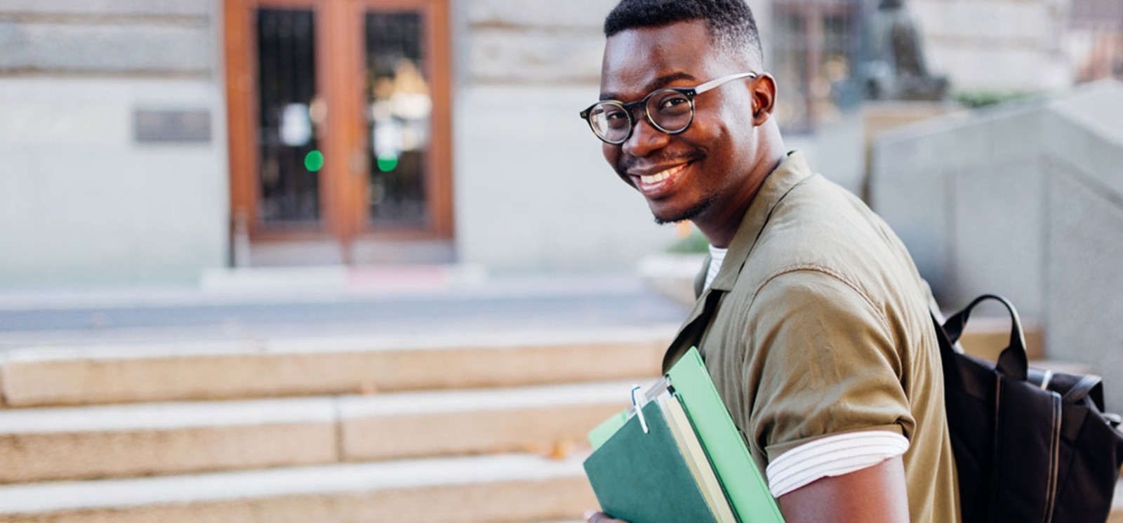 Student on campus holding books and backpack smiling.