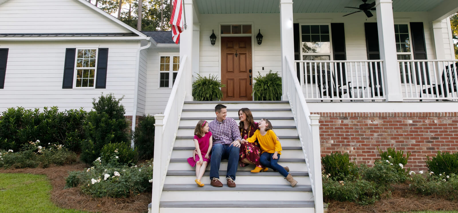 A young family sitting on the steps of a large house