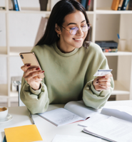 Woman in glasses holding card and phone with notebooks on table