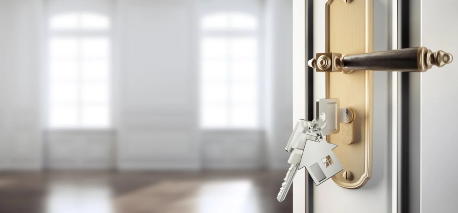 Keys in front door of home with door open looking into an empty room